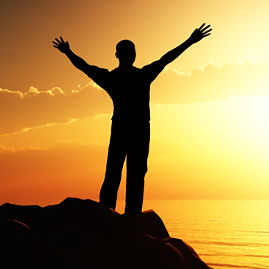 silhouette of a man reaching up against an orange sunset and water